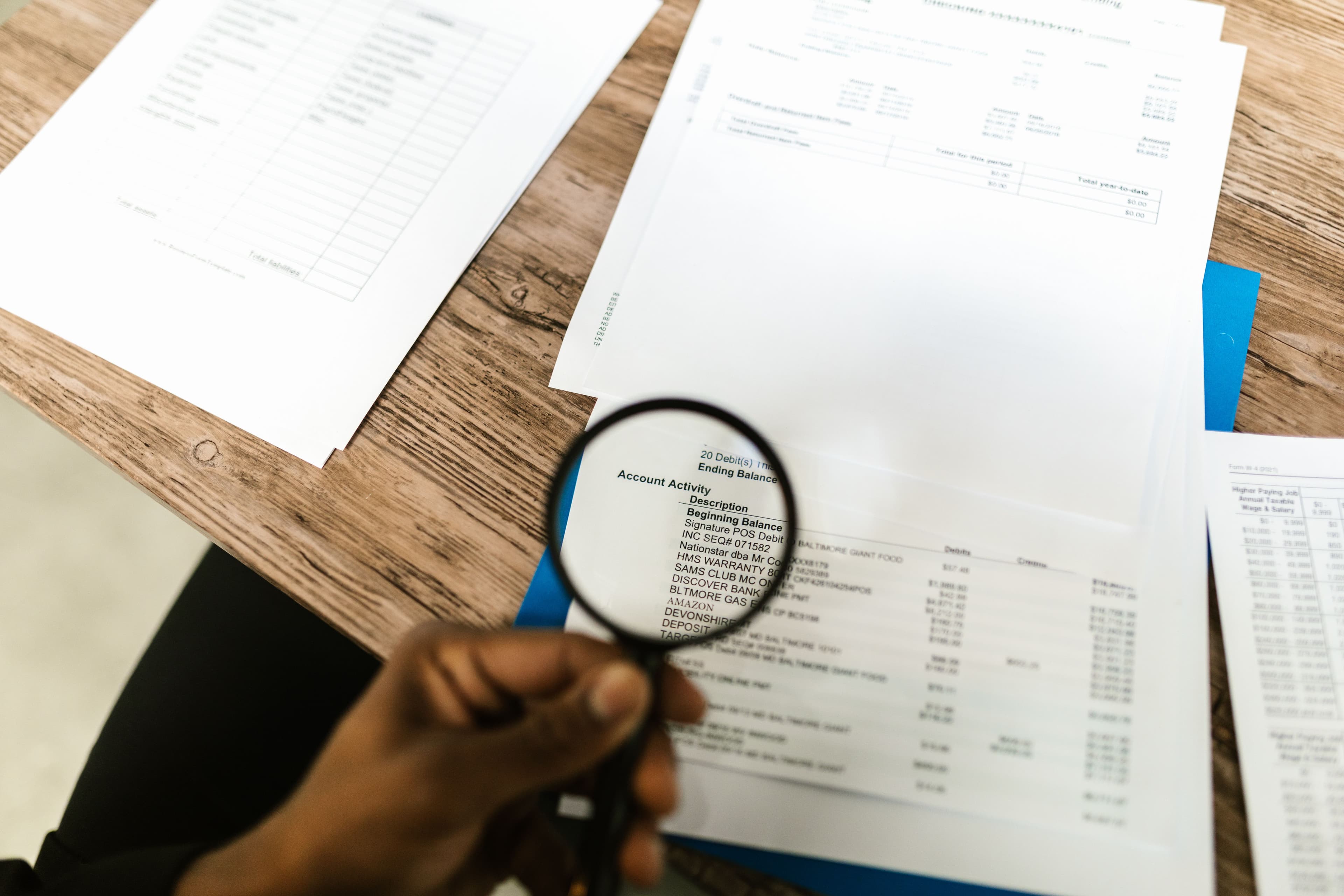 A hand holding a magnifying glass over a printed document on a desk